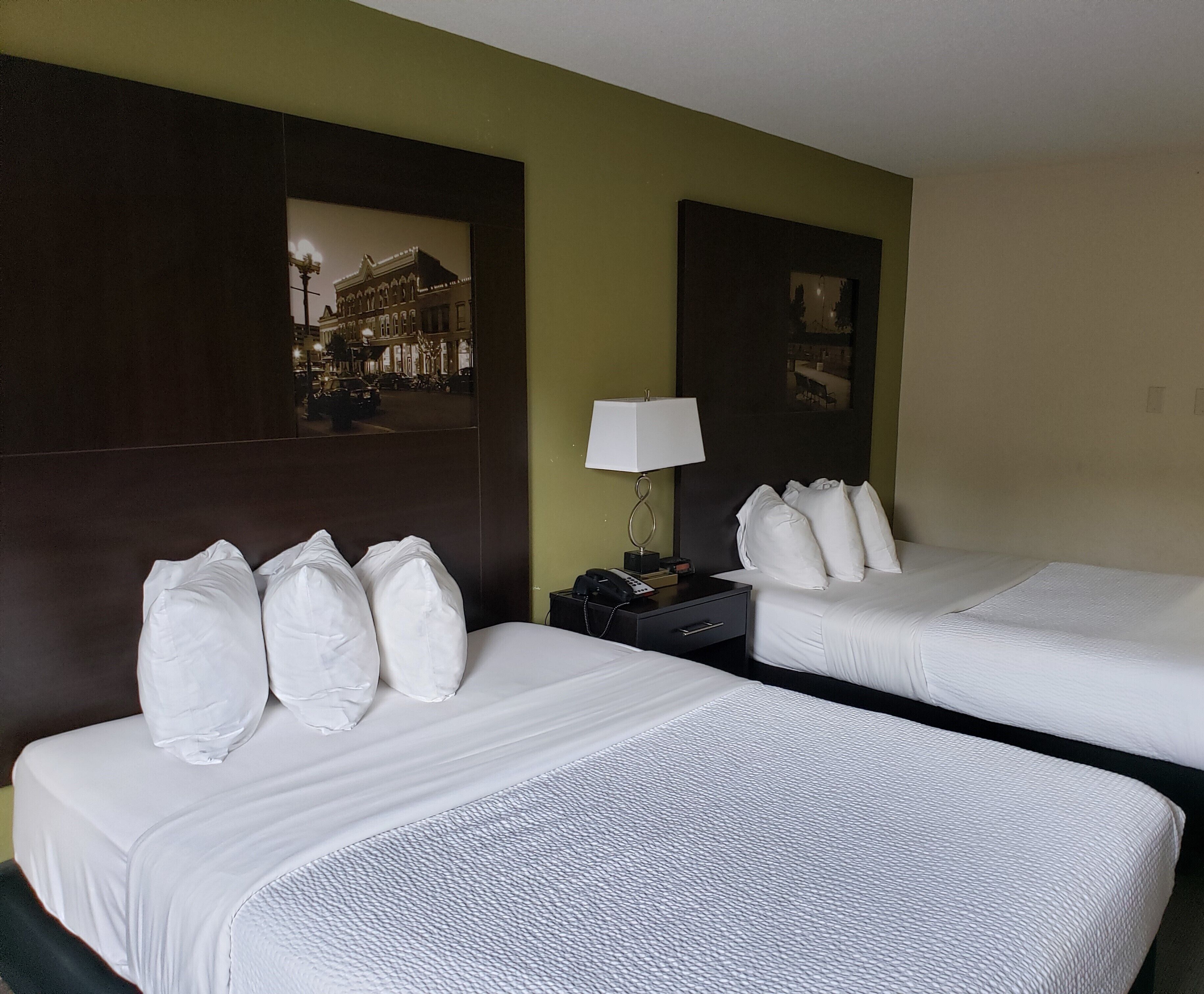 Une chambre d’hôtel avec deux lits, une table de chevet avec une lampe et un tableau encadré au mur.