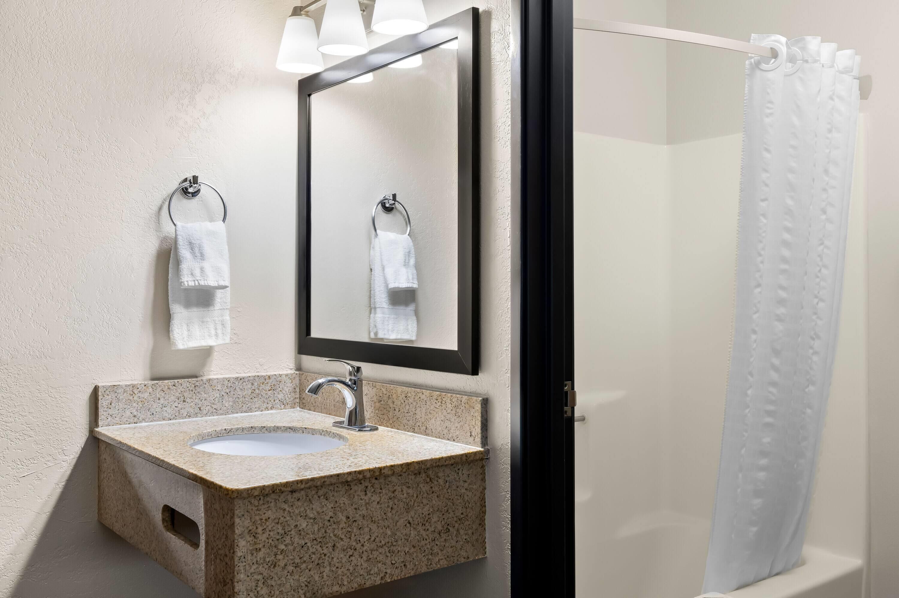 A bathroom with a granite sink, a mirror, and a shower curtain.