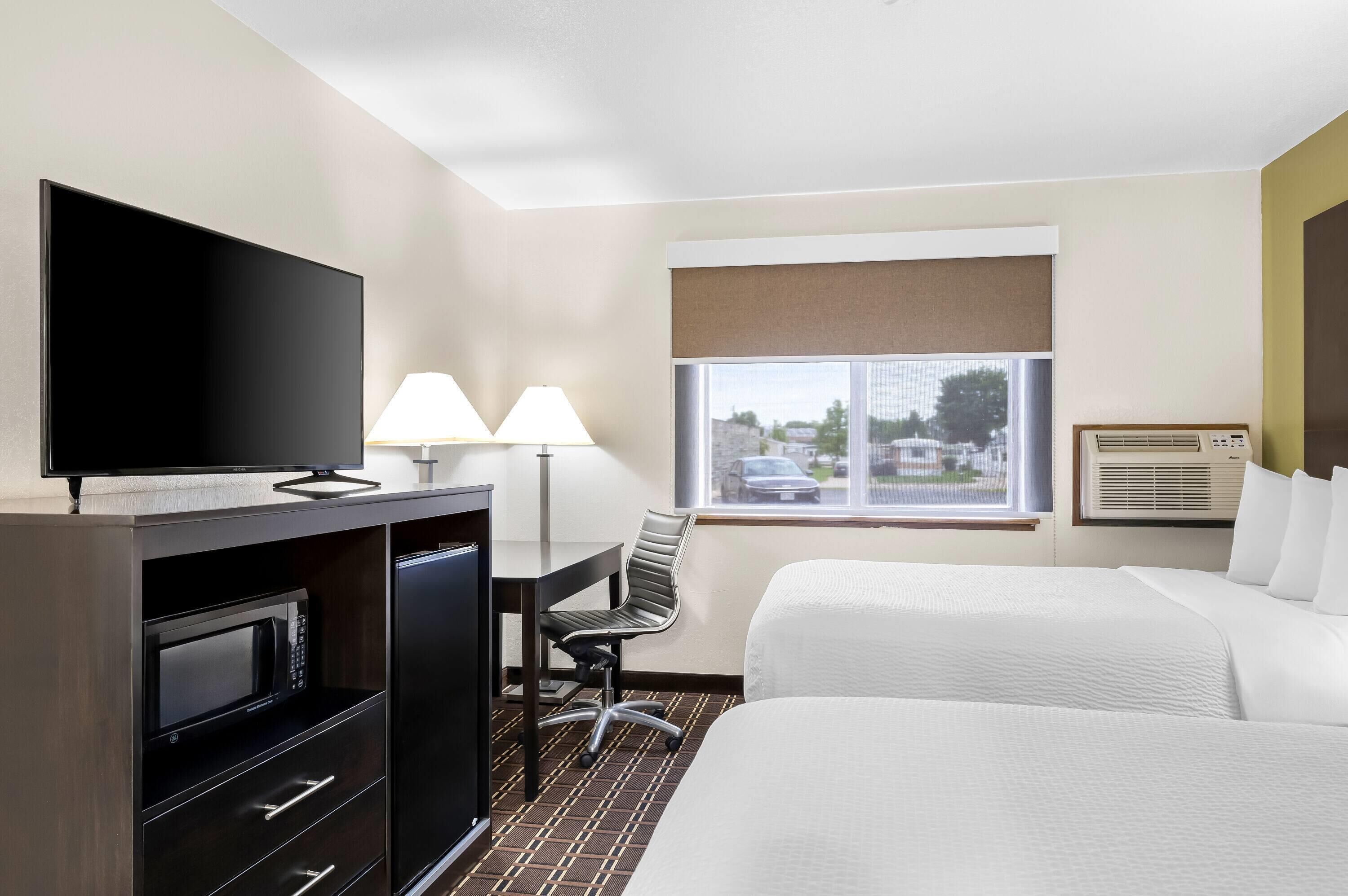 Habitación de hotel con cama, escritorio con lámpara, televisión, microondas y aire acondicionado.