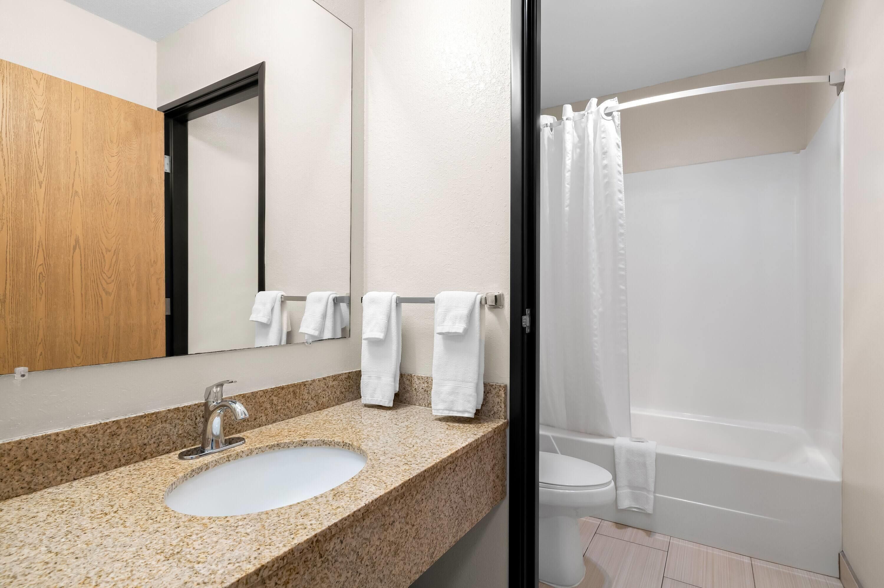 A bathroom with a granite countertop sink, a mirror, and a shower with a white curtain.