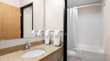 A bathroom with a granite countertop sink, a mirror, and a shower with a white curtain.