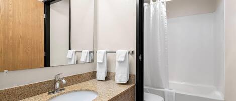 A bathroom with a granite countertop sink, a mirror, and a shower with a white curtain.