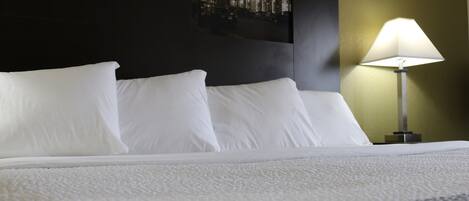 A neatly made bed with white linens, a lamp on the side, and a framed picture on the wall.