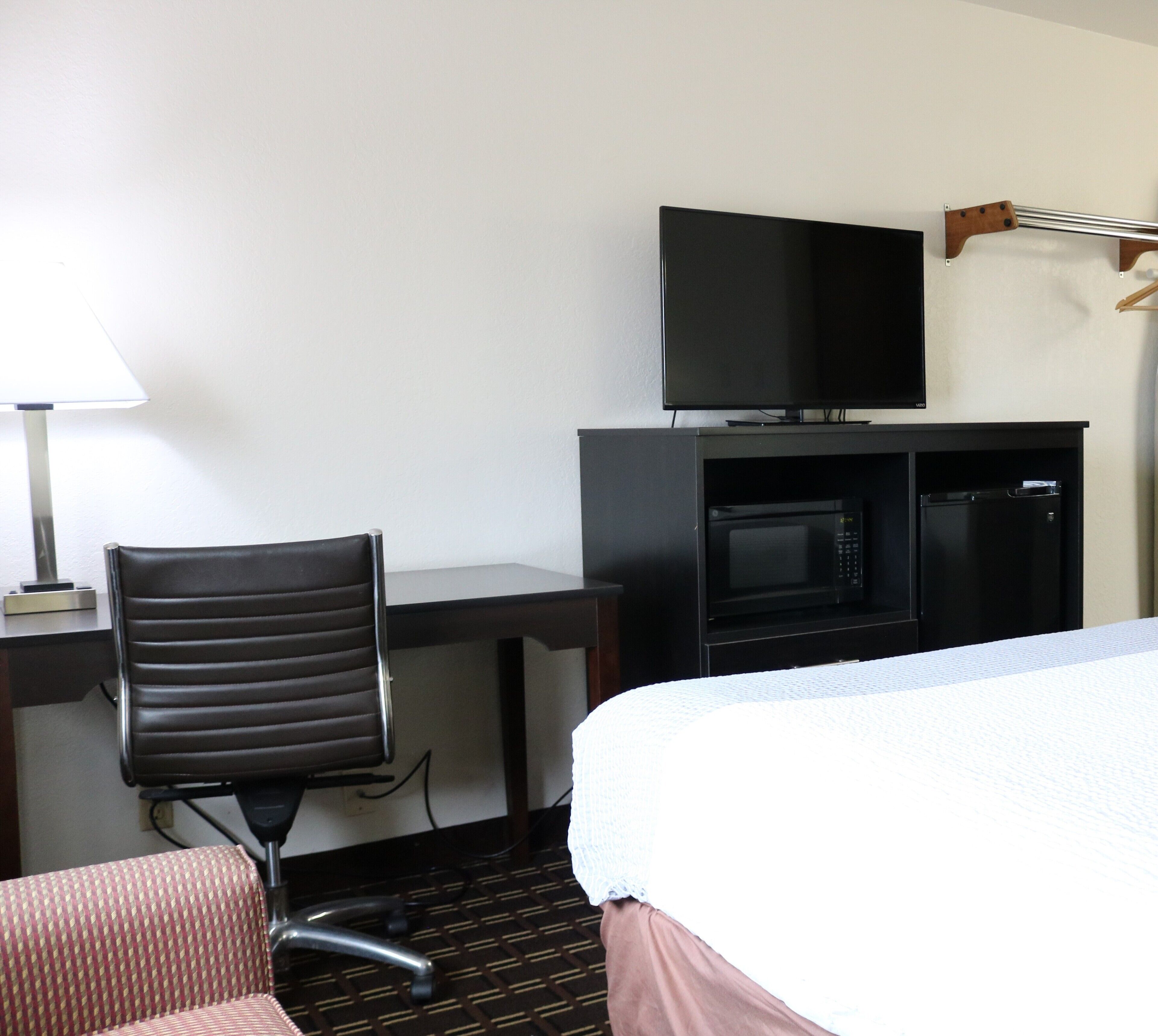 A hotel room with a bed, a desk with a television, a microwave, and a chair.
