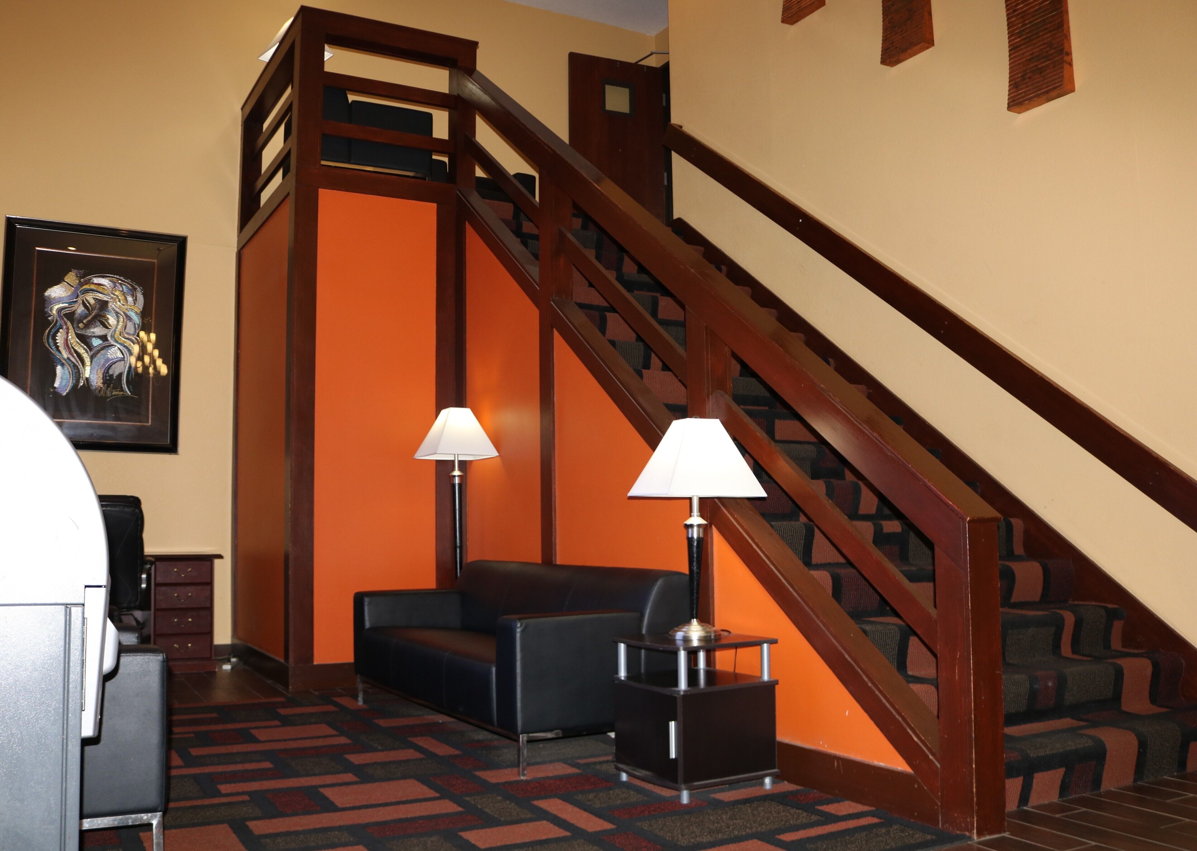 Un hall d’hôtel avec un escalier, un canapé, deux lampes et une œuvre d’art encadrée accrochée au mur.