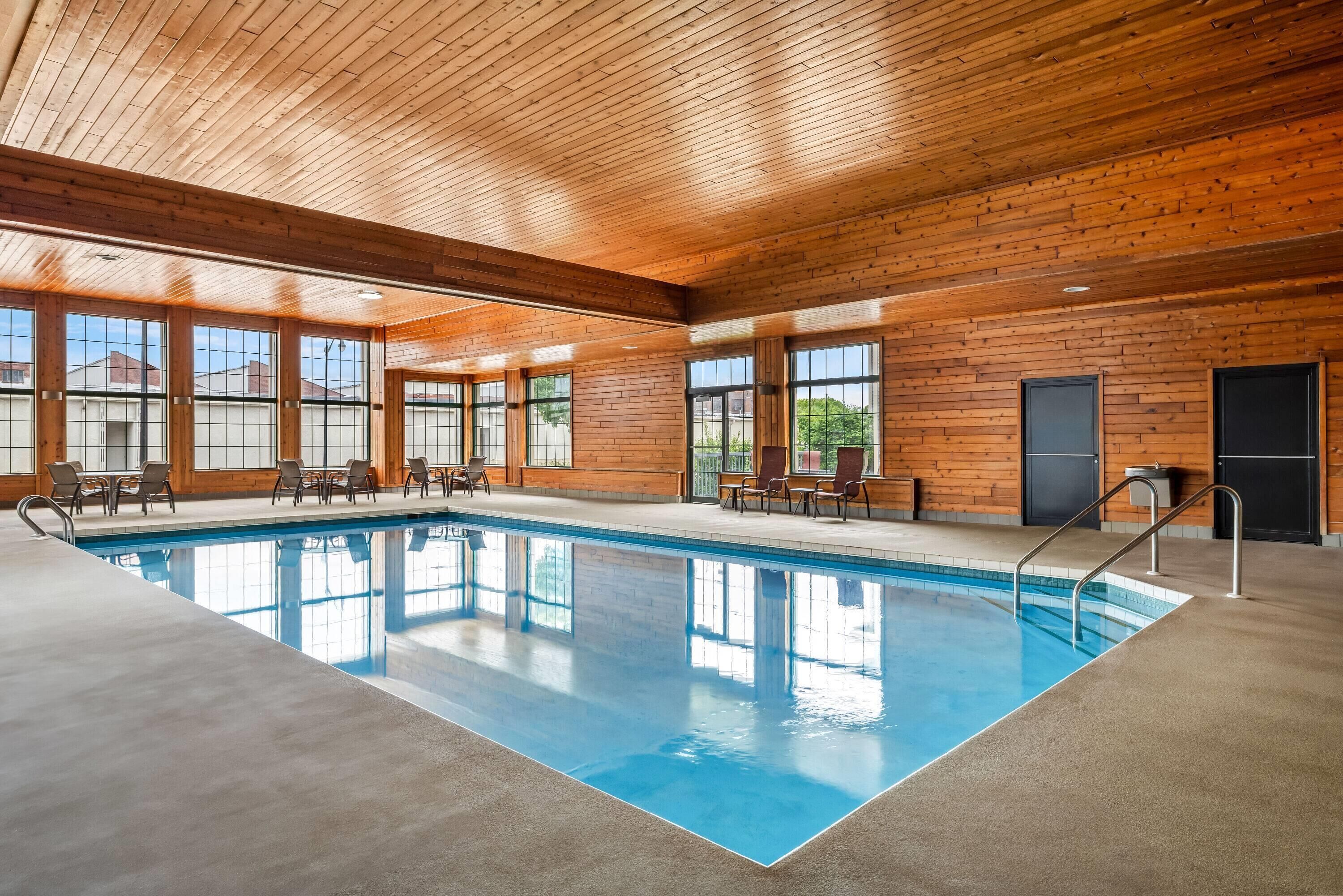 An indoor swimming pool with wooden walls and ceiling, surrounded by chairs and tables.
