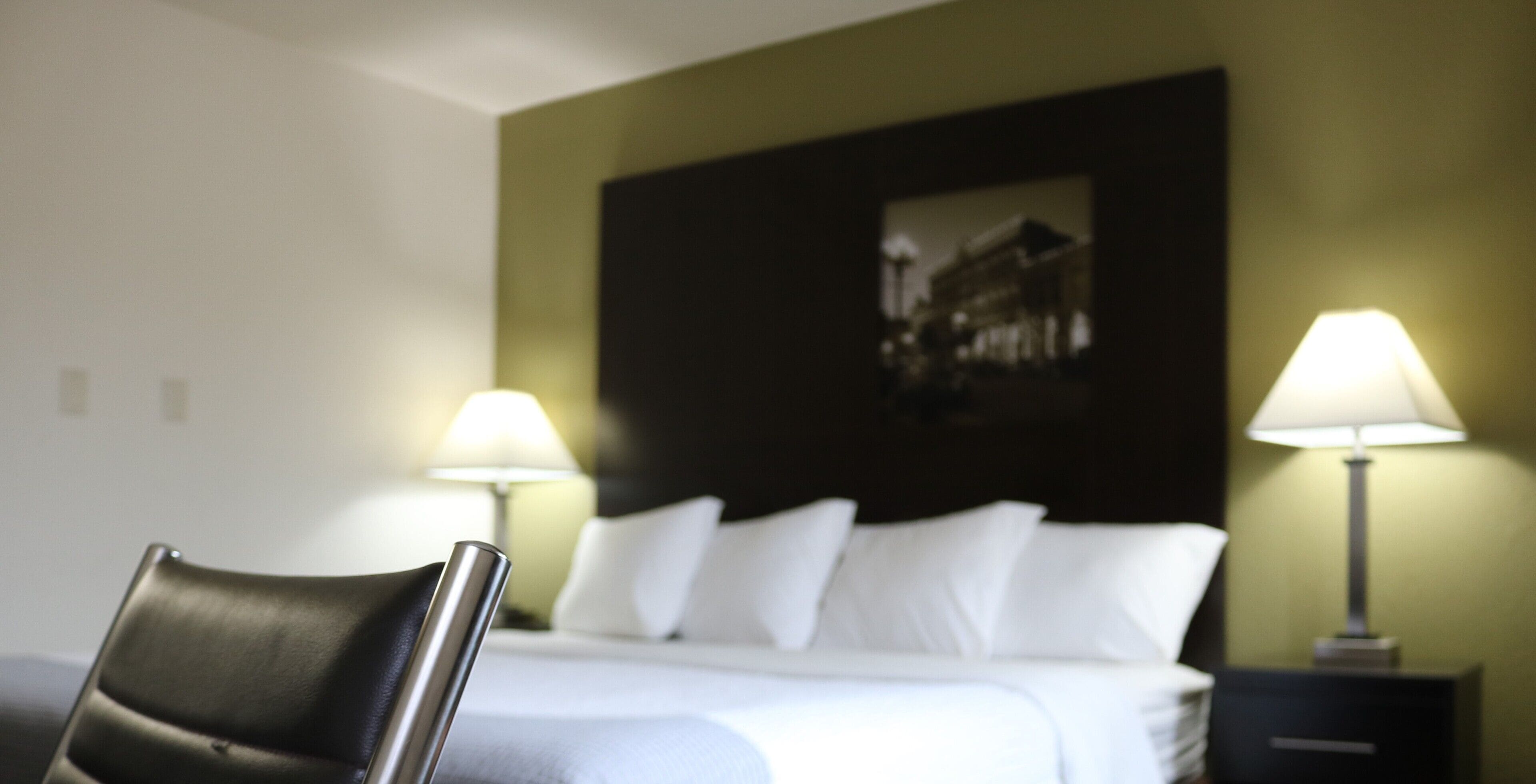 A hotel room with a bed, two bedside lamps, a chair, and a wall-mounted picture.