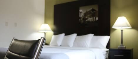 Una habitación de hotel con cama, dos lámparas de noche, una silla e imagen colgada en la pared.