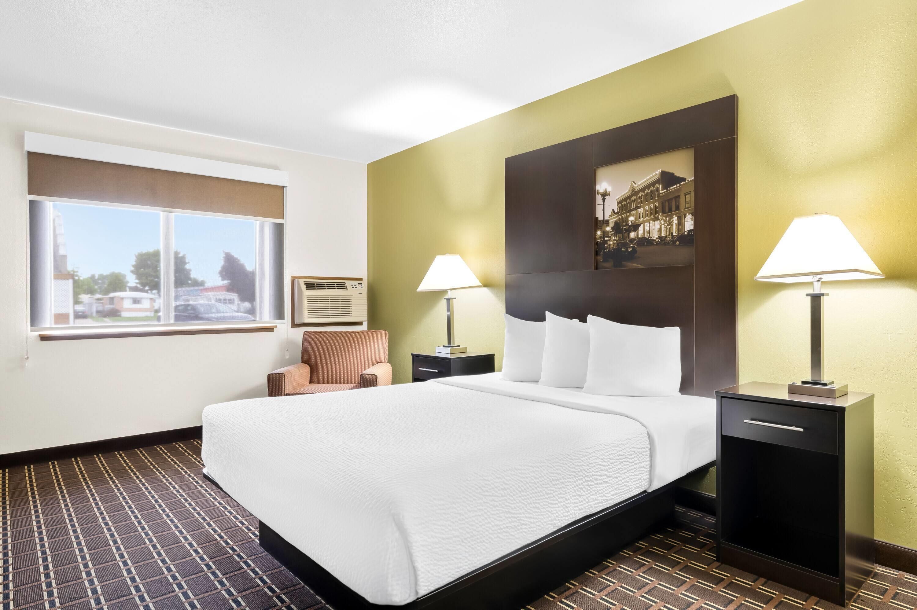 A hotel room with a large bed, two bedside tables with lamps, a window with a view, and a wall-mounted picture.