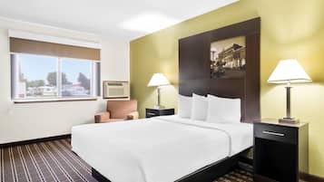 A hotel room with a large bed, two bedside tables with lamps, a window with a view, and a wall-mounted picture.