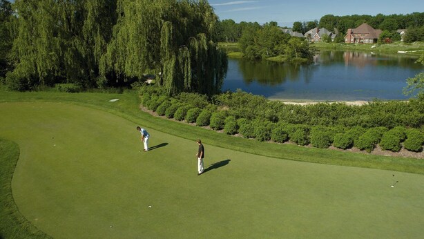 A golf course with a pond, trees, and houses in the background. - Inn On Woodlake (Kohler)