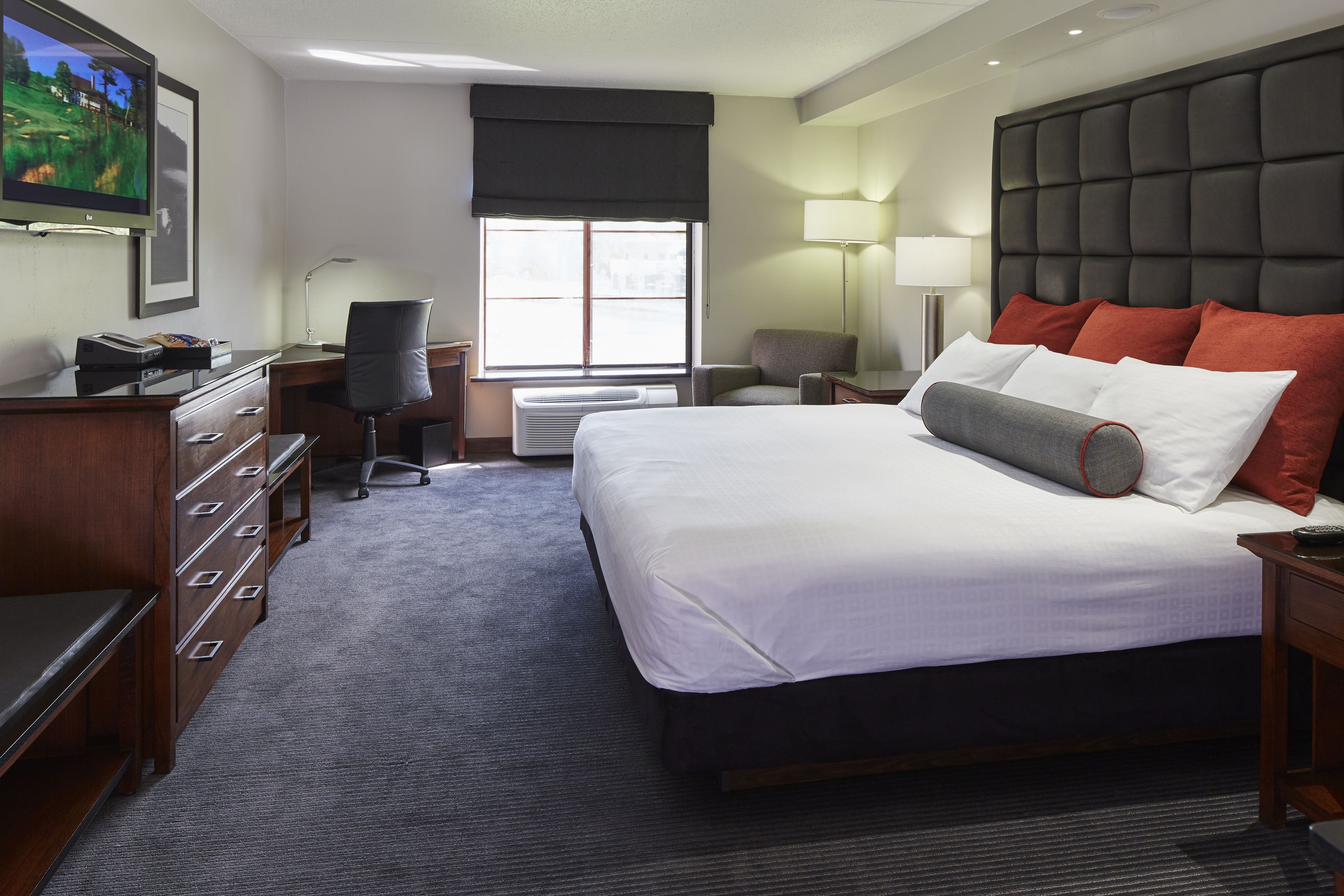 A hotel room with a large bed, a desk with a computer, a chair, a TV, and a window with a view.