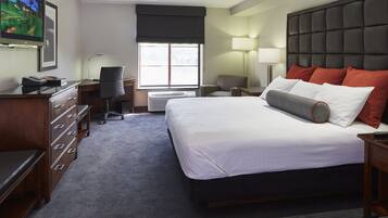 A hotel room with a large bed, a desk with a computer, a chair, a TV, and a window with a view.