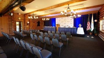 Uma sala de conferências com fileiras de cadeiras, um palanque, uma bandeira americana e um painel de fundo com logotipos 'USA'.