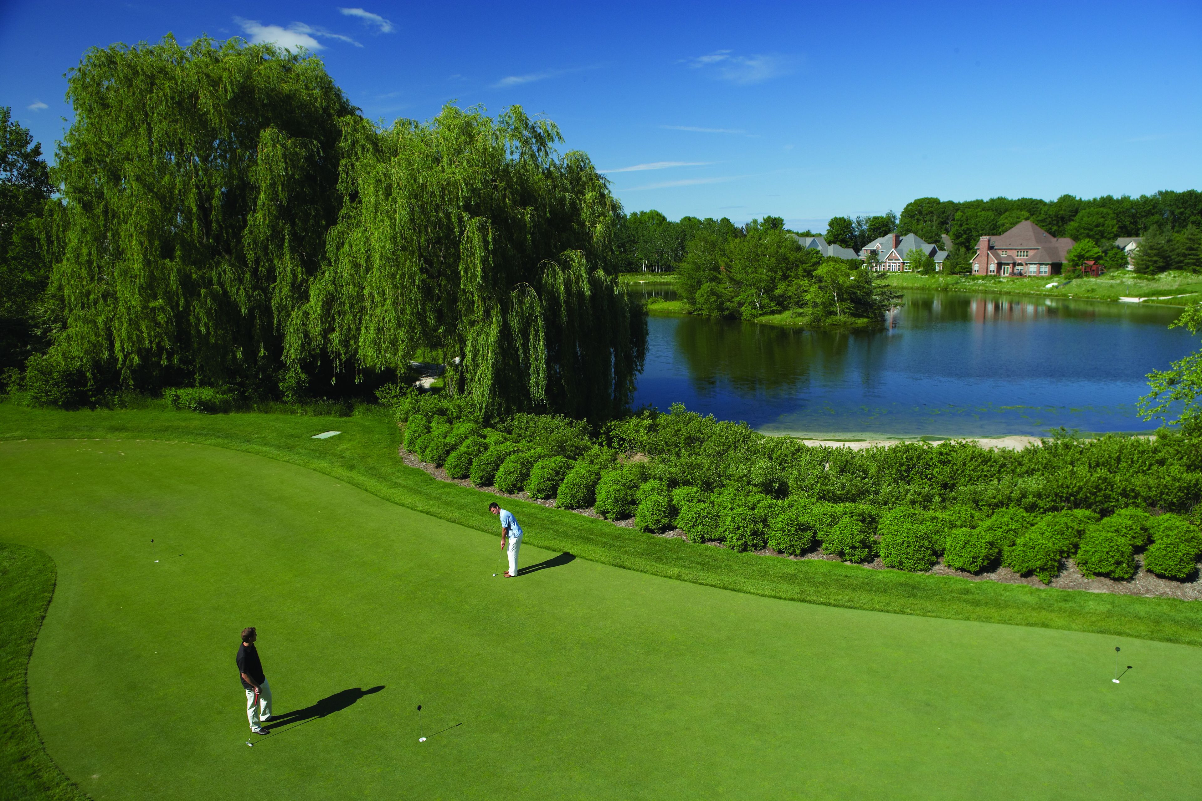 Un campo de golf con un estanque y casas al fondo.