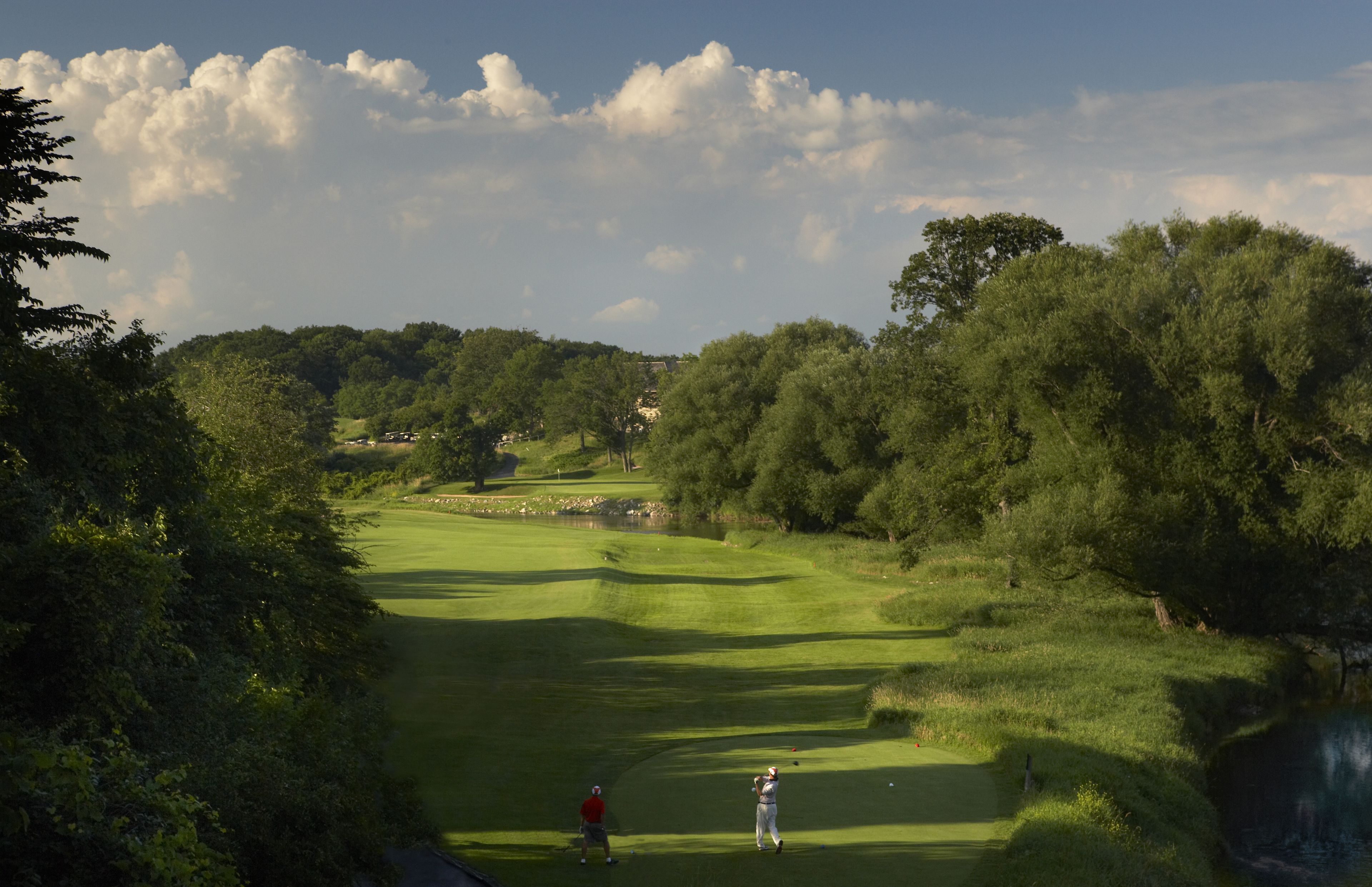 Un campo de golf con un estanque, árboles y un edificio a lo lejos.