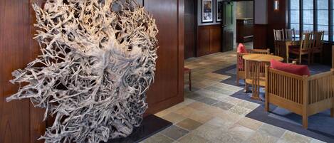 Een lobby met een grote abstracte sculptuur, een eetgedeelte met houten meubels en een betegelde vloer.
