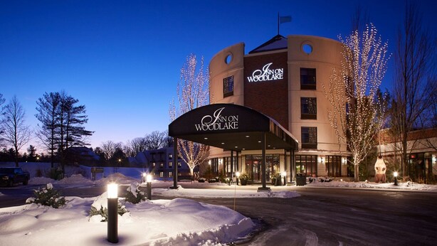 A hotel with a curved facade, illuminated signage, and snow-covered surroundings. - Inn On Woodlake (Kohler)