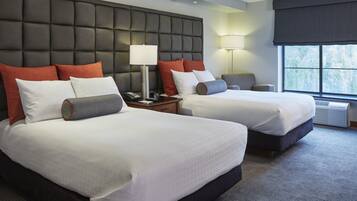 A hotel room with two beds, a large padded headboard, bedside lamps, a desk, and a view of the outdoors.