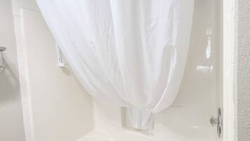 Una bañera blanca con cortina de ducha, una toalla y un grifo de cromo.