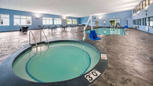 An indoor swimming pool with a 30 ft depth, surrounded by chairs and tables, and a lifeguard stand. - AmericInn by Wyndham Green Bay Near Stadium (Green Bay)