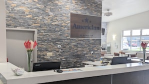 A reception desk with a stone wall backdrop, a sign reading "AmericInn By Wyndham", and a vase with red flowers. - AmericInn by Wyndham Green Bay Near Stadium (Green Bay)