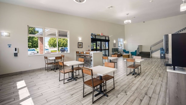 A spacious dining area with multiple tables and chairs, large windows, and a staircase leading to an upper level. - AmericInn by Wyndham Green Bay Near Stadium (Green Bay)