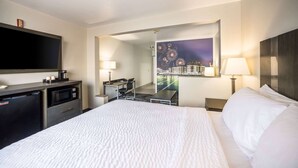 A hotel room with a bed, a desk with a chair, a television, a microwave, and a night view of a cityscape. - AmericInn by Wyndham Green Bay Near Stadium (Green Bay)