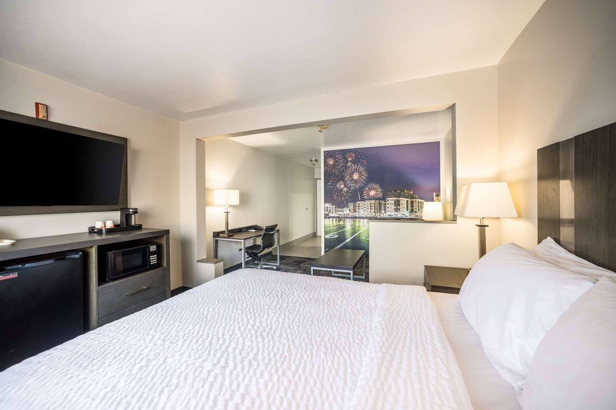 Habitación de hotel con cama, escritorio con silla, televisor, microondas y vista nocturna de un paisaje urbano.
