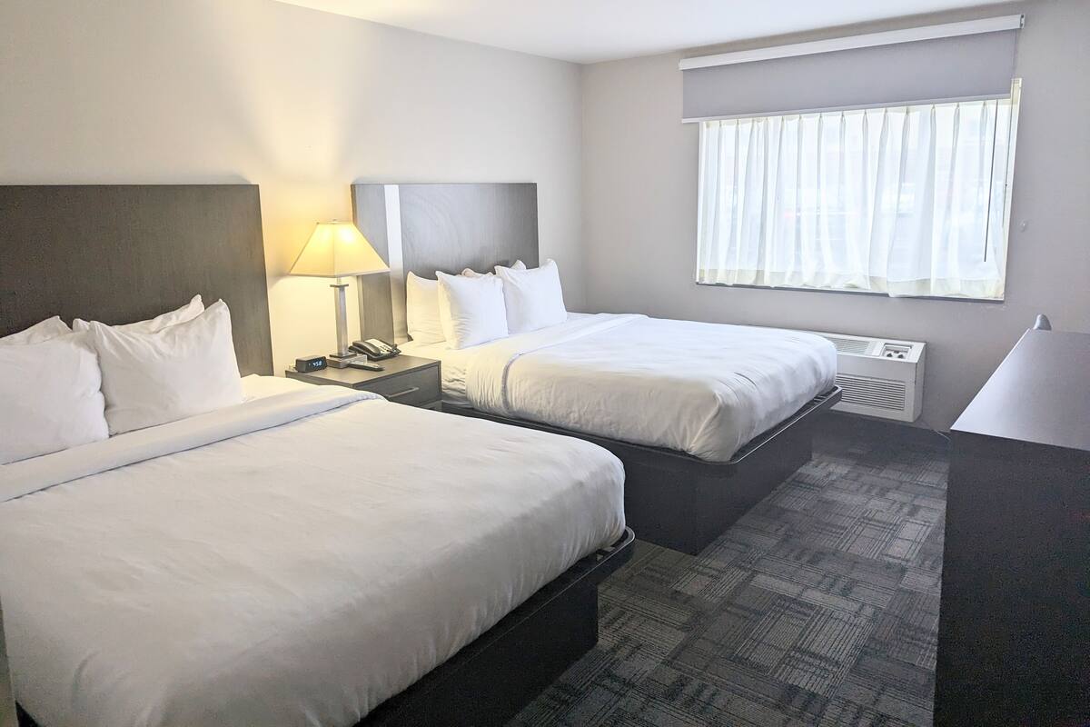 Habitación de hotel con dos camas, una mesita de noche con lámpara, teléfono y ventana con cortinas.