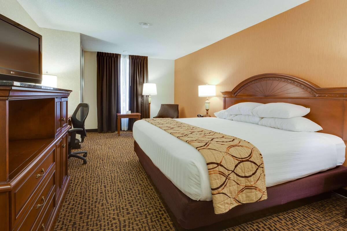 A hotel room with a large bed, a desk with a chair, a TV, and a lamp.
