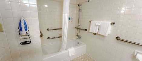 A bathroom with a bathtub, shower, and handrails.
