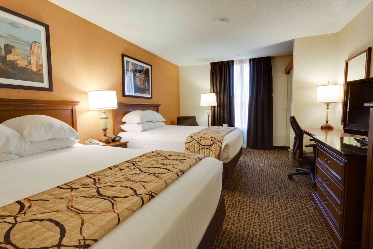 A hotel room with two beds, a desk, a chair, a dresser, and a TV.