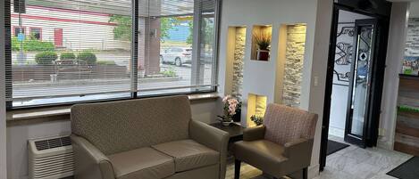 Un vestíbulo moderno con un sofá color beige, un sillón pequeño y una mesa con plantas decorativas.