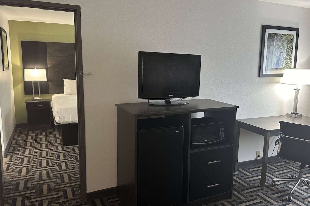 A hotel room with a bed, a desk with a computer, a television, and a small refrigerator.