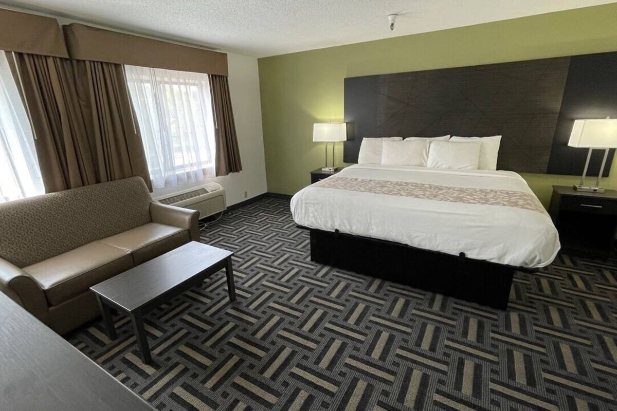 A hotel room with a bed, a sofa, a small table, two bedside lamps, and a window with curtains.