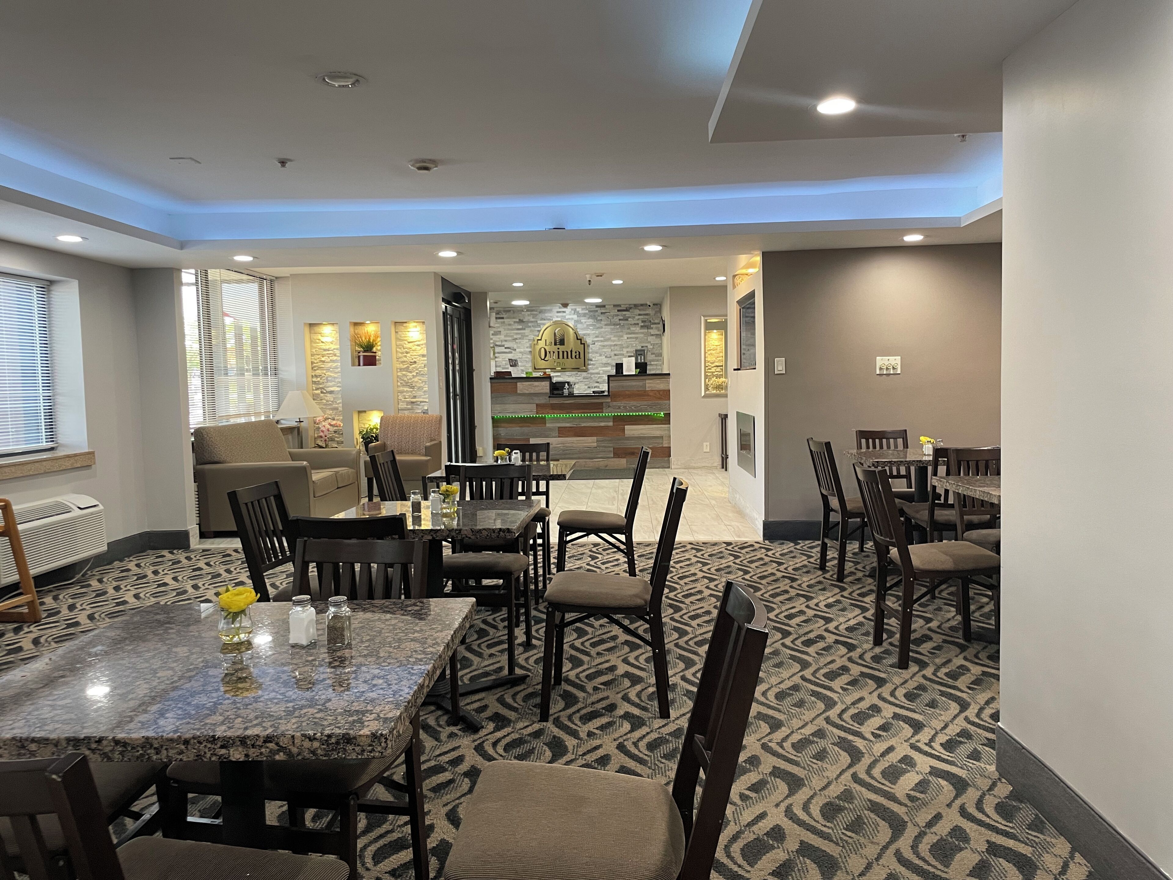 A hotel lobby with a reception desk, seating area, and a dining area with tables and chairs.