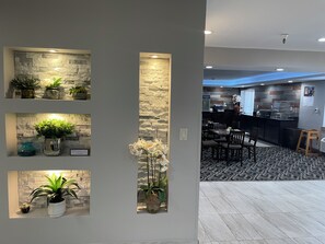 A modern interior with a stone accent wall, potted plants, and a kitchen area with a counter and seating. - La Quinta Inn and Suites by Wyndham Cincinnati North (Cincinnati)