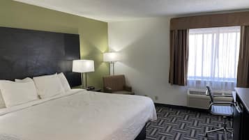 A hotel room with a large bed, a chair, a desk, a lamp, and a window with curtains.