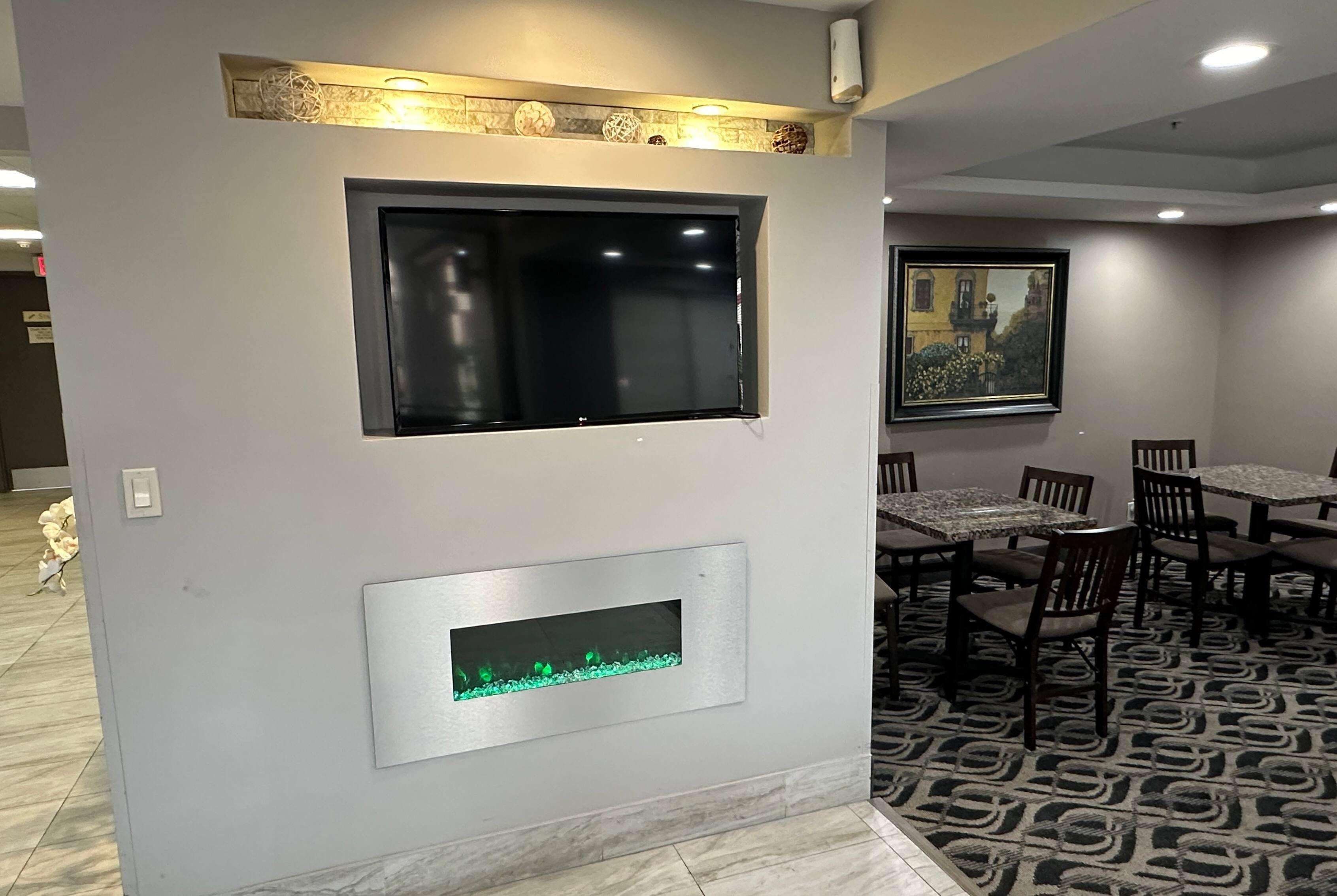 Un comedor con mesas y sillas, una chimenea y un televisor montado en la pared.