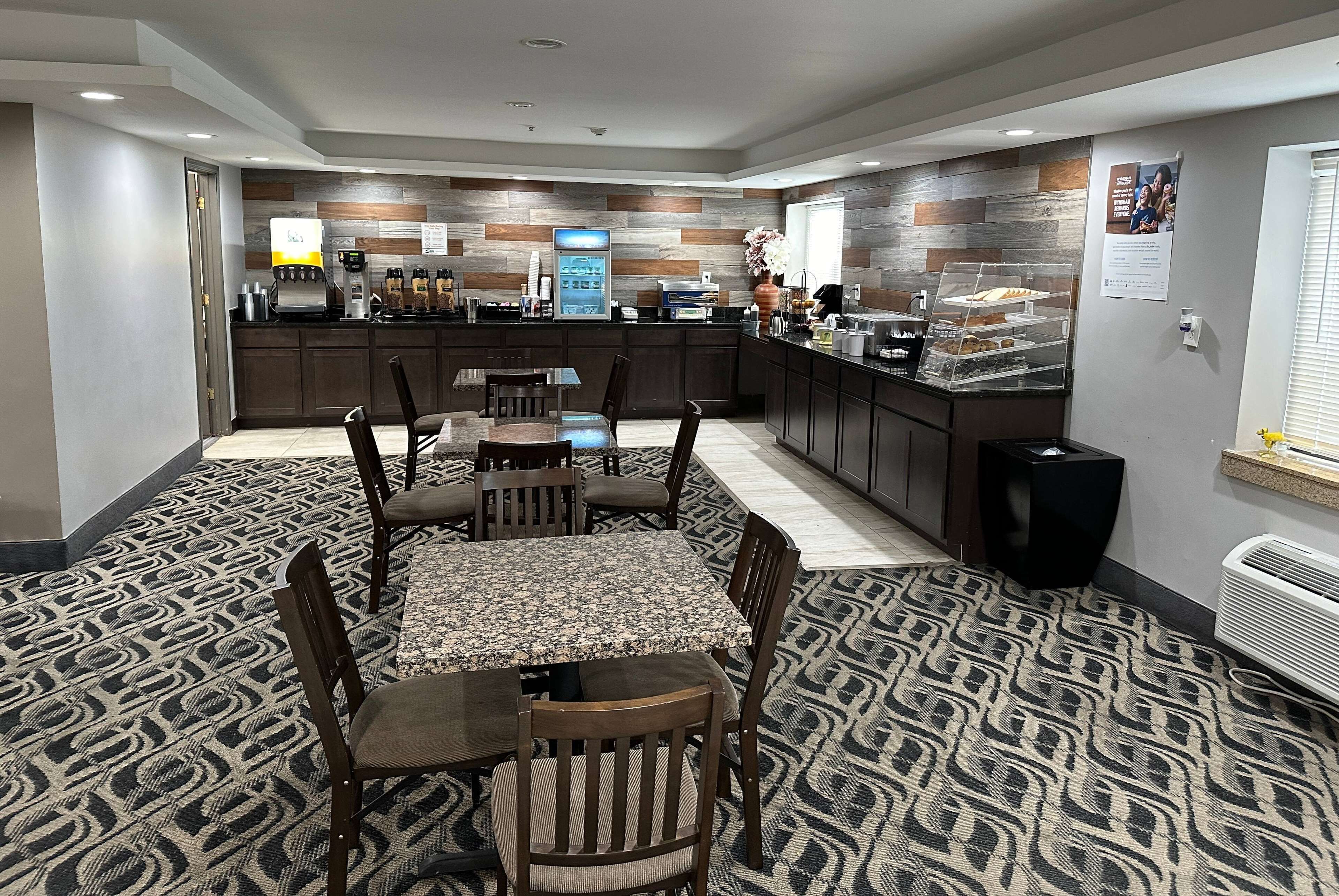 Habitación de hotel con comedor que incluye una mesa y sillas, una cocina con cafetera y refrigerador, y una alfombra estampada.