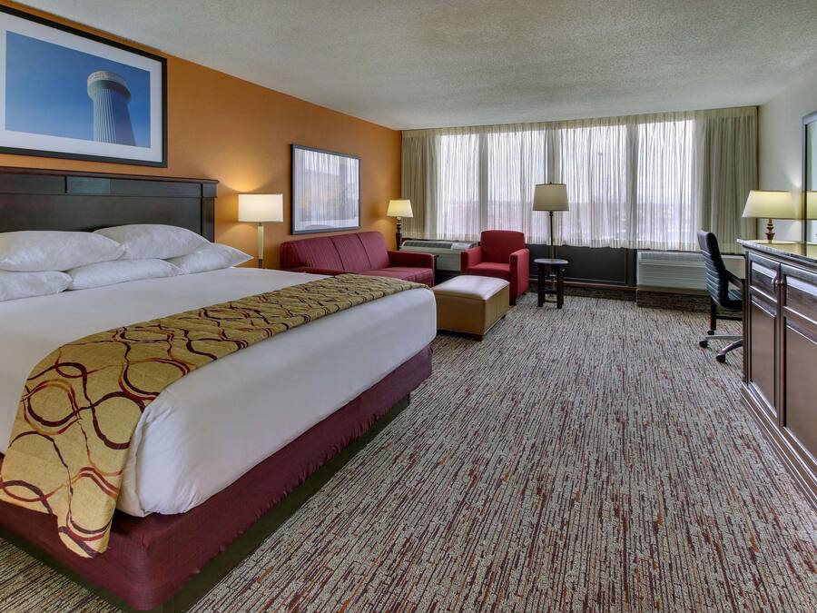 A hotel room with a large bed, a desk with a chair, a TV, and a window with curtains.