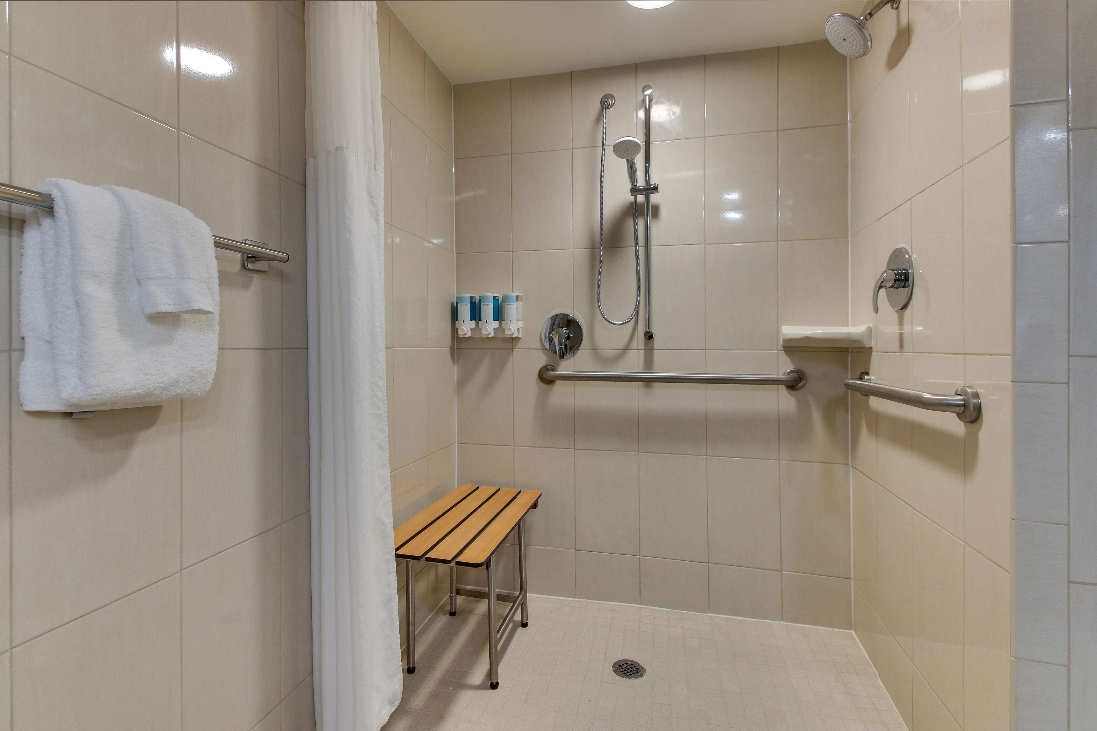 A shower area with a bench, grab bars, and a towel rack.