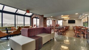A modern indoor space with a large window, a seating area with sofas and chairs, and a dining area with tables and chairs. - Pear Tree Inn St. Louis Arnold (Arnold)