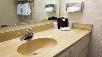 A bathroom with a large beige sink, a mirror, and two paper towel dispensers.