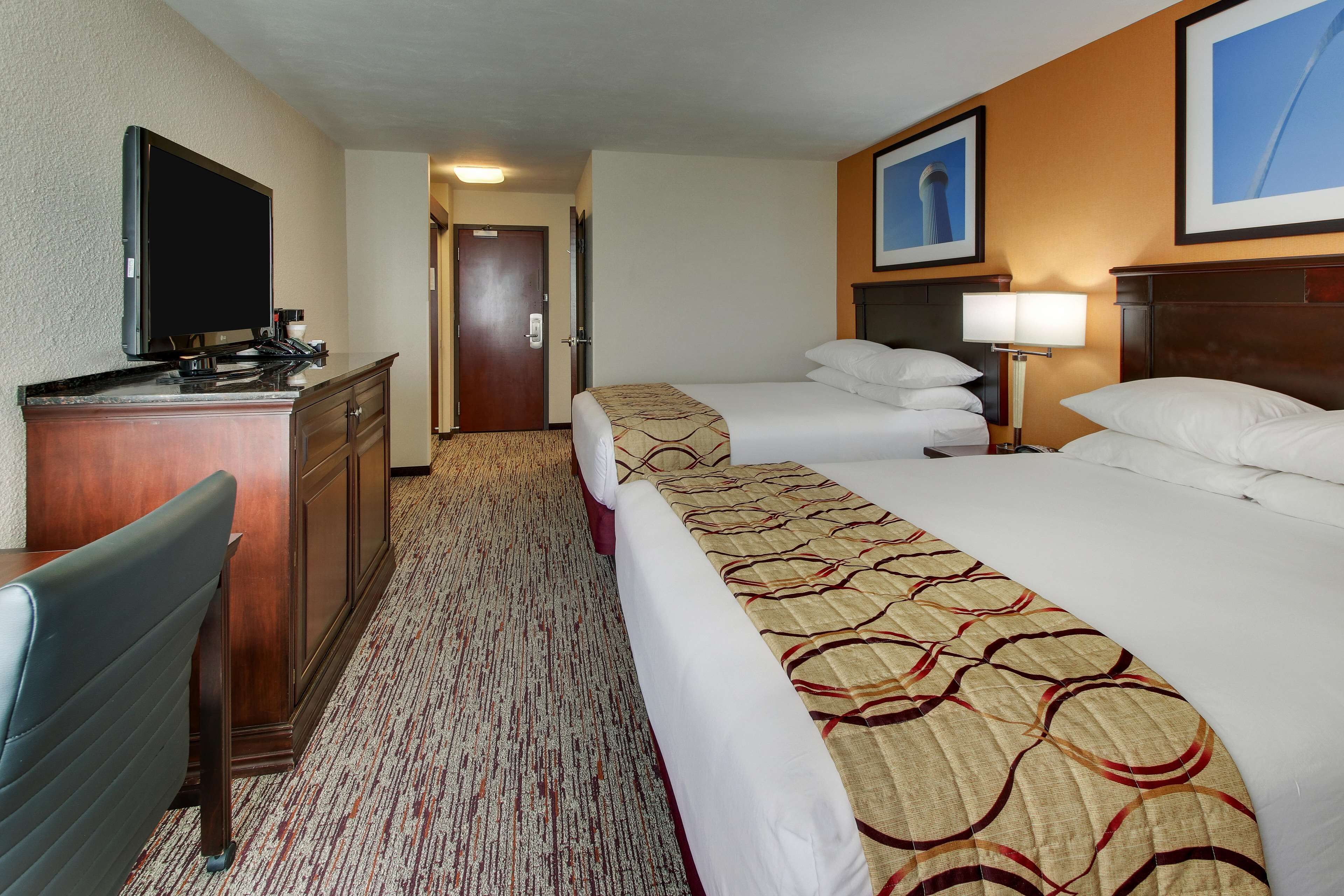 A hotel room with a bed, a desk with a television, a lamp, and a door leading to another room.