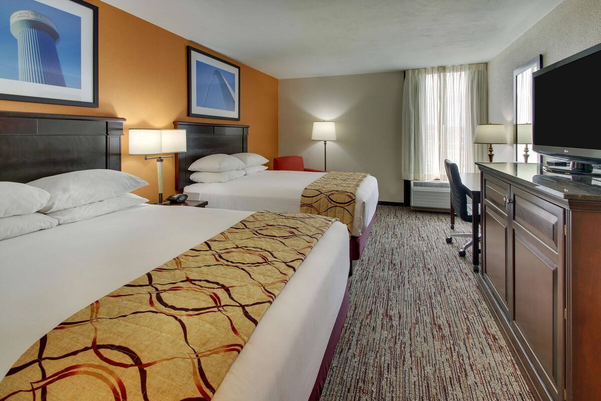 A hotel room with two beds, a desk, a TV, and a lamp.