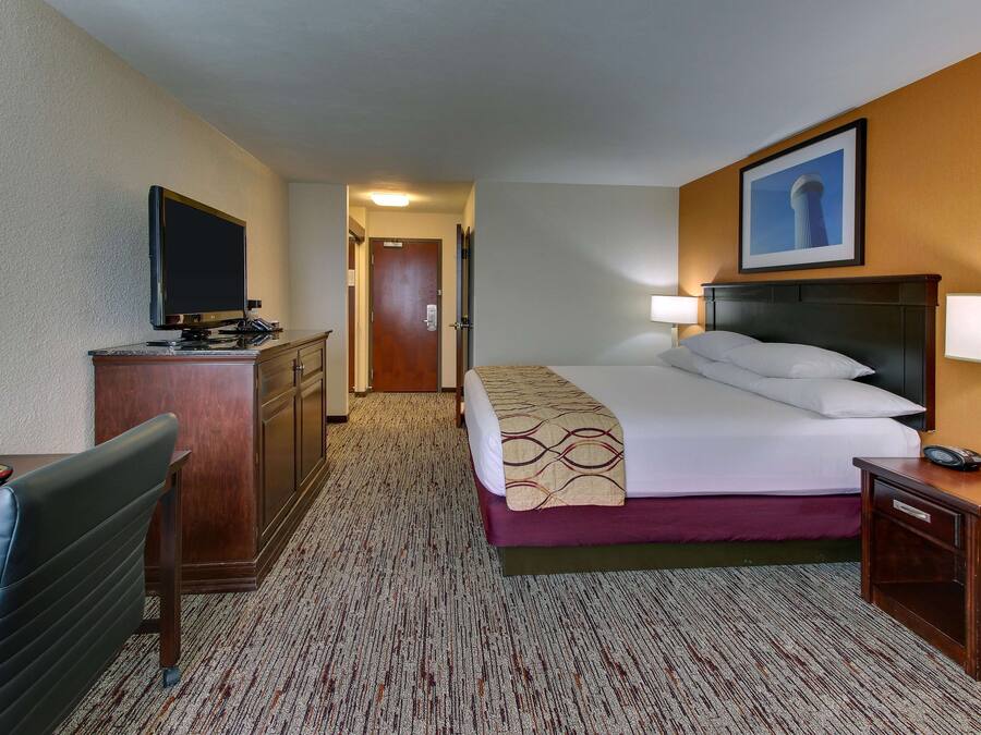 A hotel room with a bed, bedside table, desk, chair, television, and a door leading to another room.