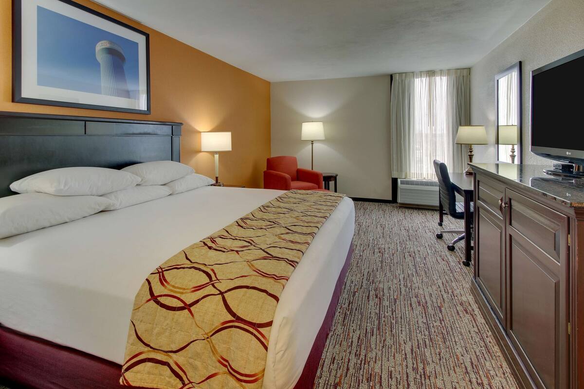 A hotel room with a large bed, a desk with a chair, a television, and two lamps.