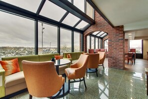 A modern interior with a high ceiling, large windows, and a brick wall. There are orange chairs and a green sofa with orange cushions. - Pear Tree Inn St. Louis Arnold (Arnold)